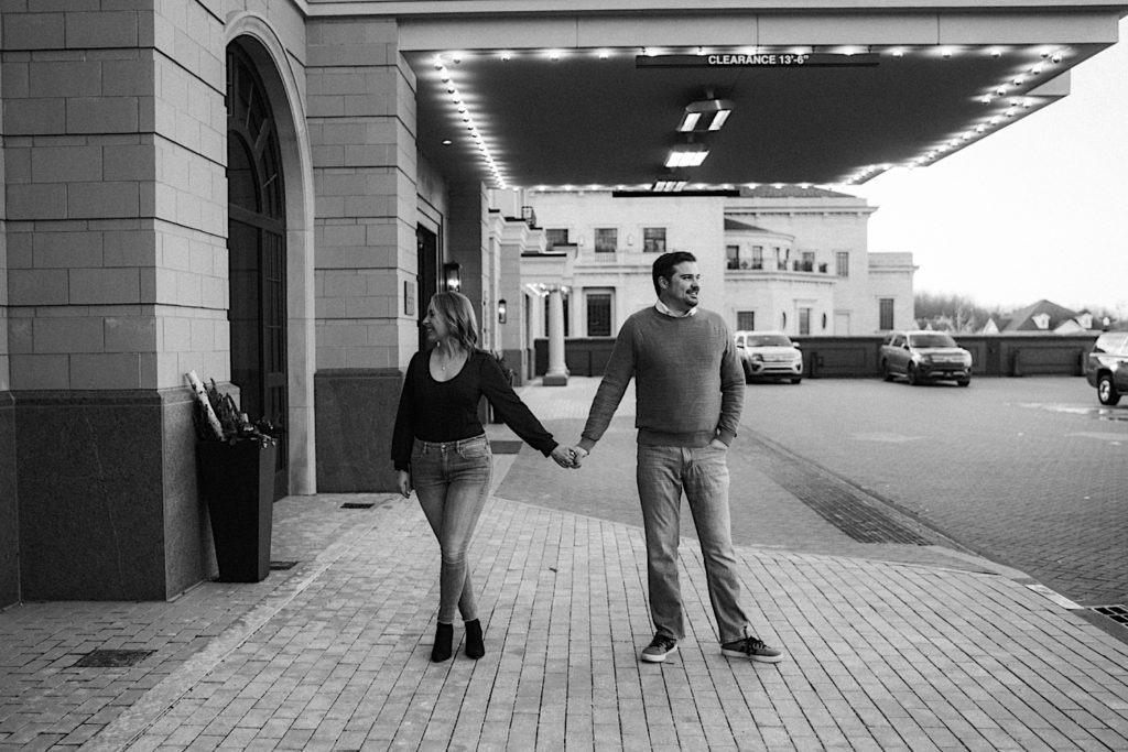 Engaged couple hold hands standing under building patio