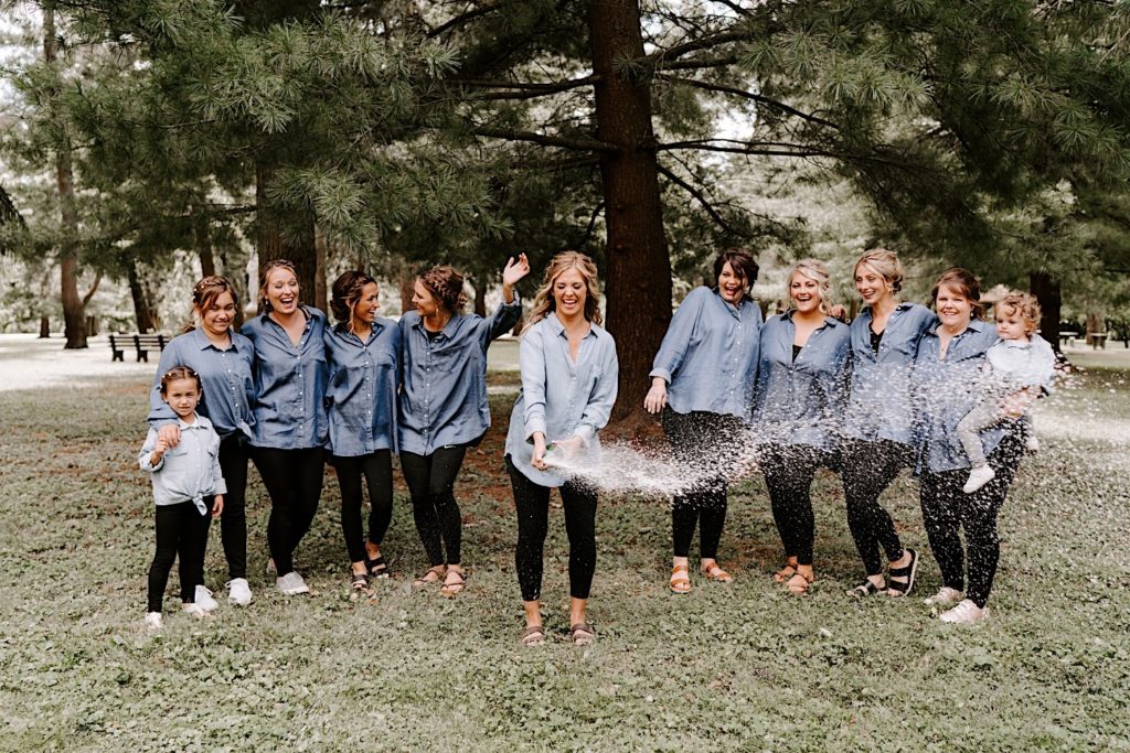 Bride popping champaign surrounded by her bridal party in denim shirts