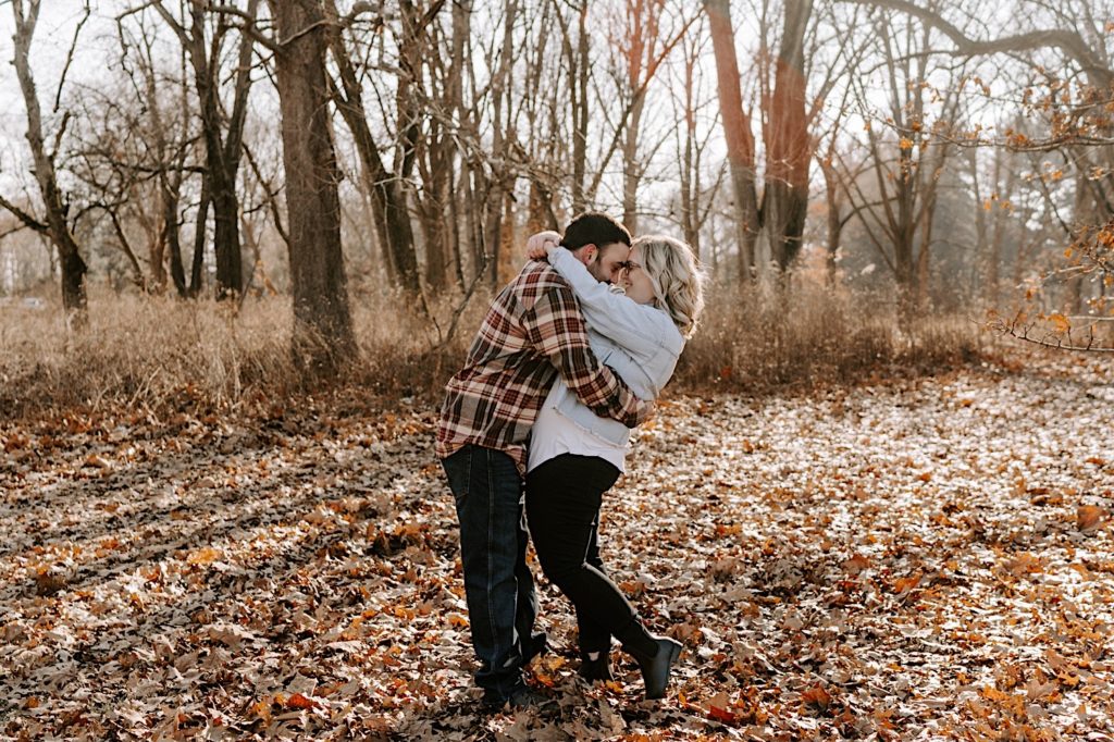 Couple embrace and smile together surrounded by fallen leaves in the fall