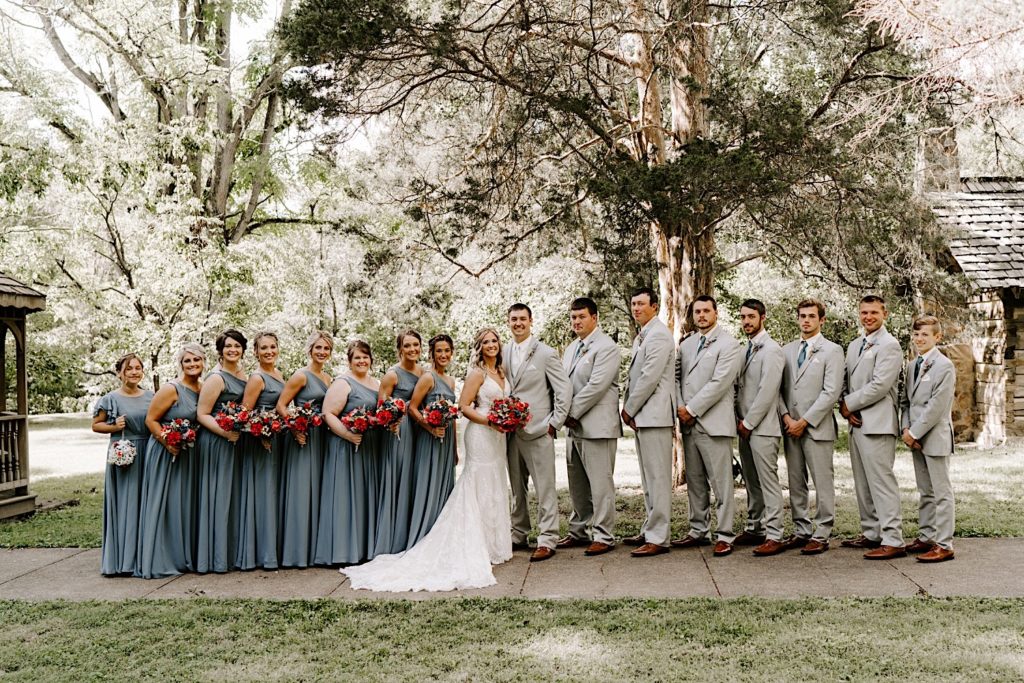 Bride and groom surrounded by bridal party and groomsmen in front of trees in Indiana wedding