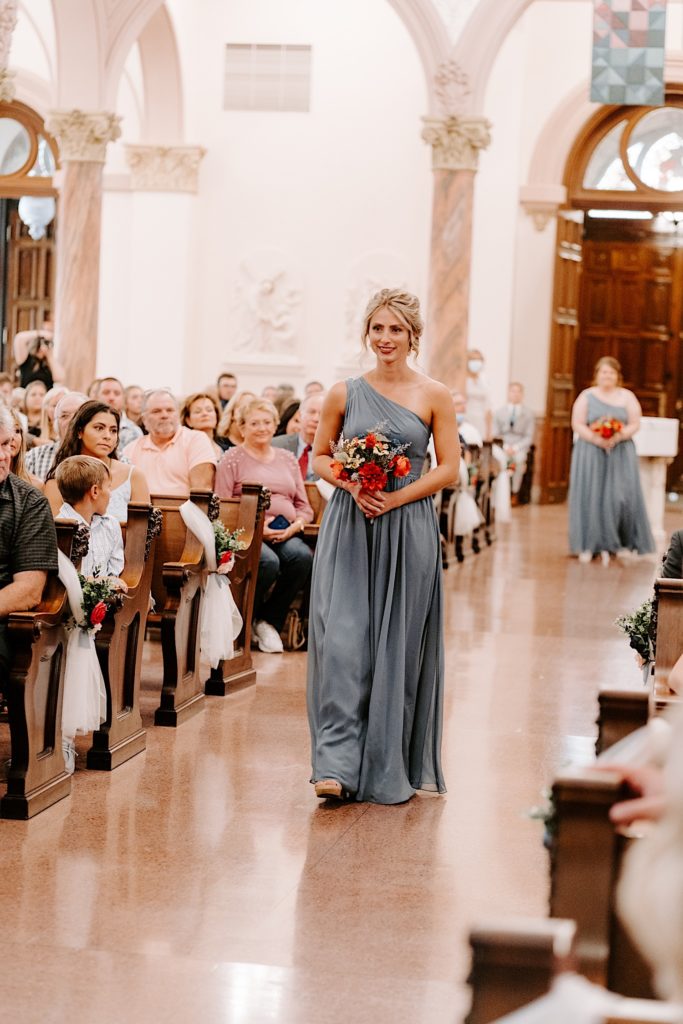 Bridesmaid walking down aisle with bouquet in Indiana church