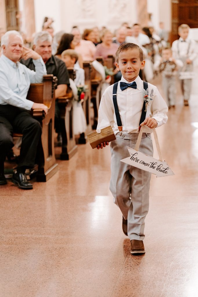 Ring bearer walking down aisle holding a "here comes the bride" sign in Indiana church