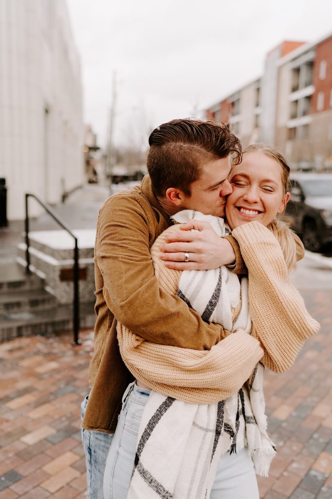 Man kisses girlfriend on the cheek in downtown while hugging her from behind