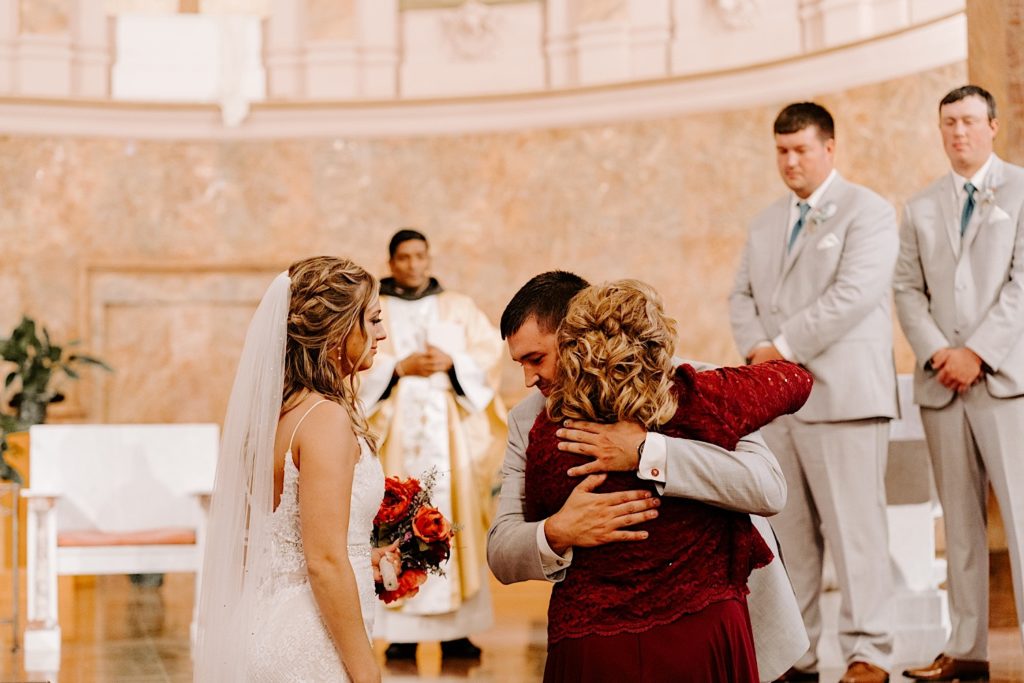 Groom embracing brides mother at alter