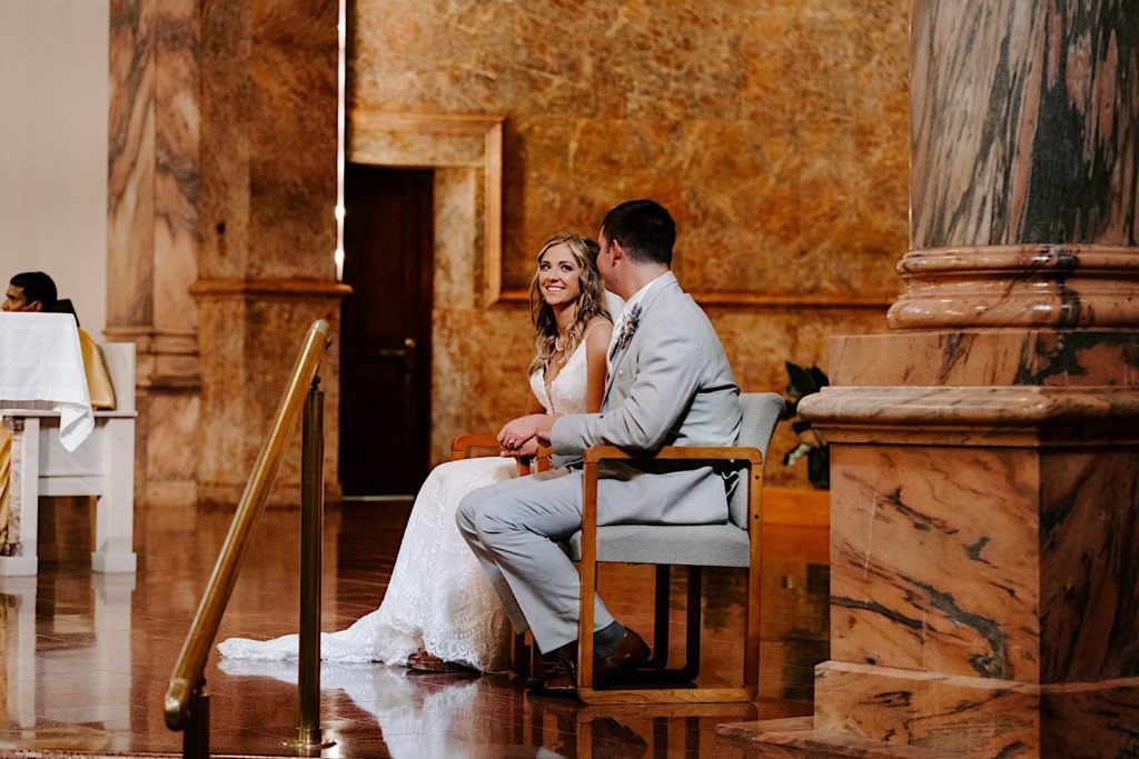 Bride and groom sitting in chairs at the alter looking at one another