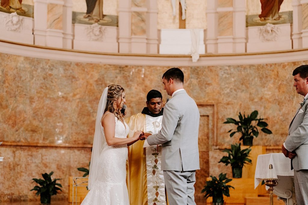 Bride and groom holding hands at alter with priest standing behind them in ornate Indiana church