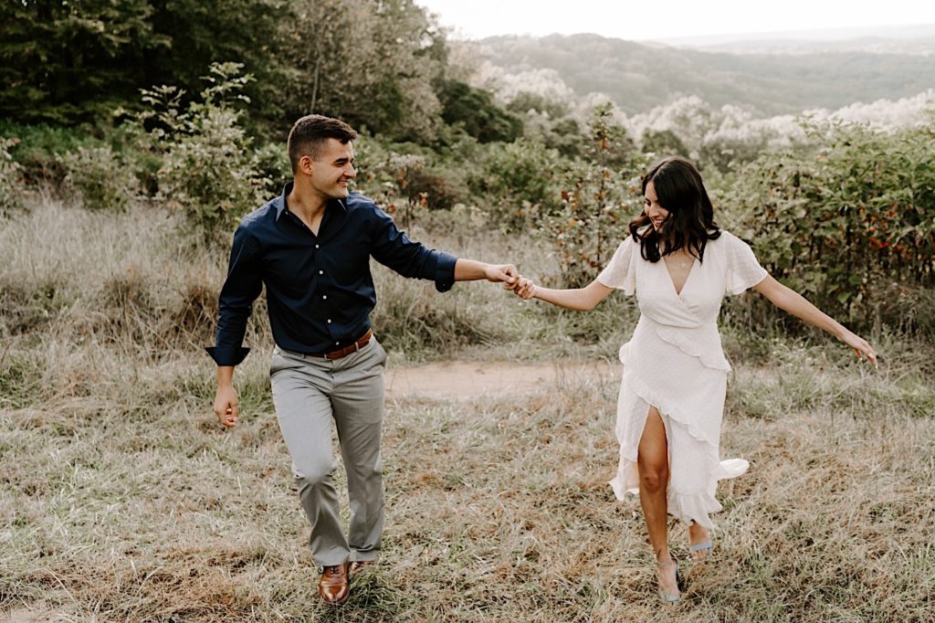 Couple walking through a field towards the camera holding hands and smiling