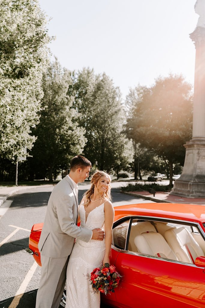 Bride and groom leaning on red car after ceremony