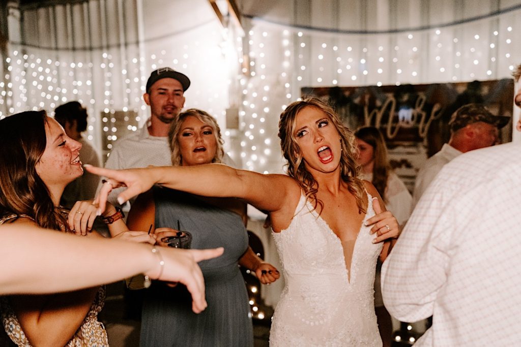 Bride dancing and pointing on dance floor surrounded by guests at reception