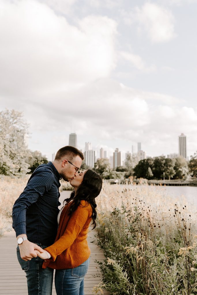 Couple kissing in Chicago's Lincoln Park while holding hands with the city skyline in the background