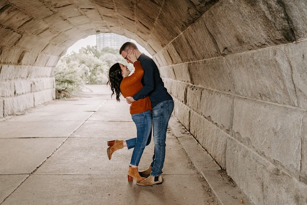 Couple holding one another and smiling at each other underneath an overpass in Chicago's Lincoln Park during their engagement session 