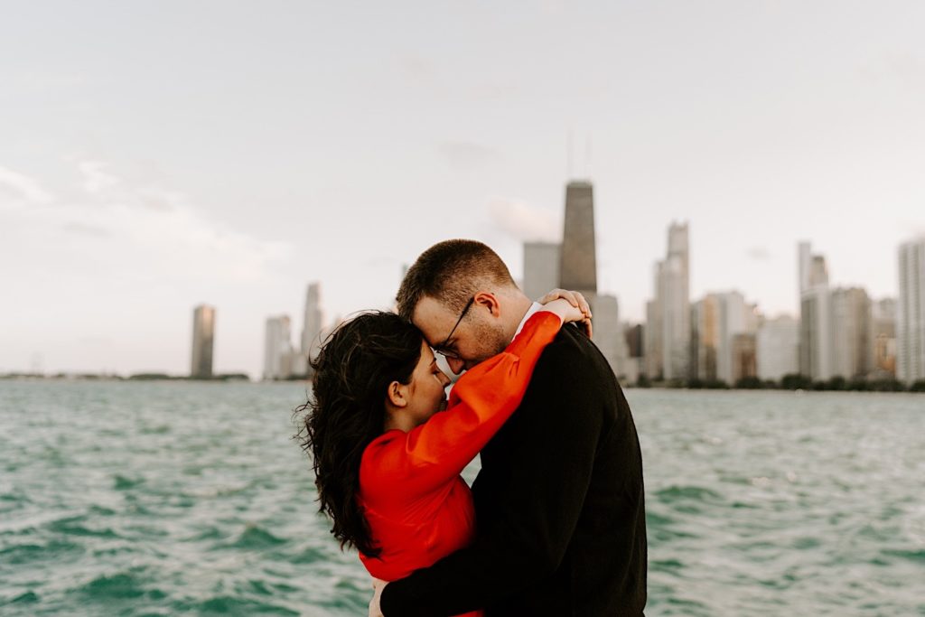 Couple embrace and touch their foreheads together at North Avenue Beach in front of Lake Michigan and the Chicago skyline during their engagement session