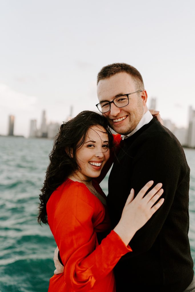 Couple embrace and smile at the camera together at North Avenue Beach in front of Lake Michigan and the Chicago skyline