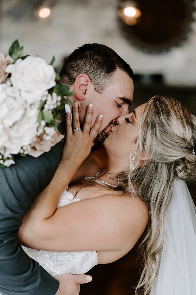 Bride holding grooms face while kissing
