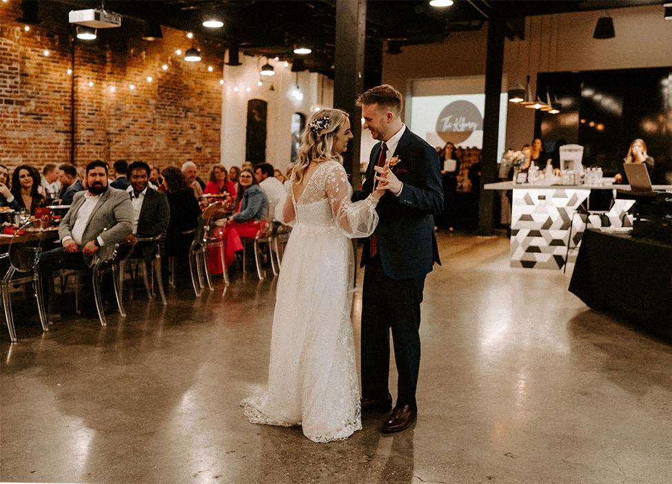 Gif of a groom kissing and dipping his bride during their first dance at their reception space while their guests clap for them