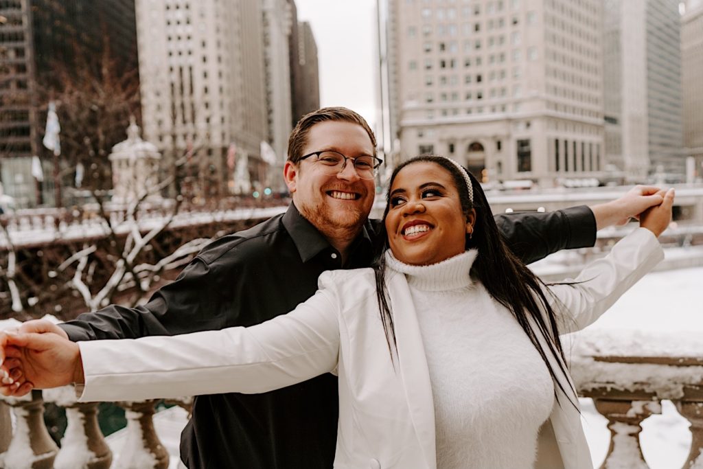 Engaged couple holding hands with their arms out like they are going to fly in Chicago winter engagement session