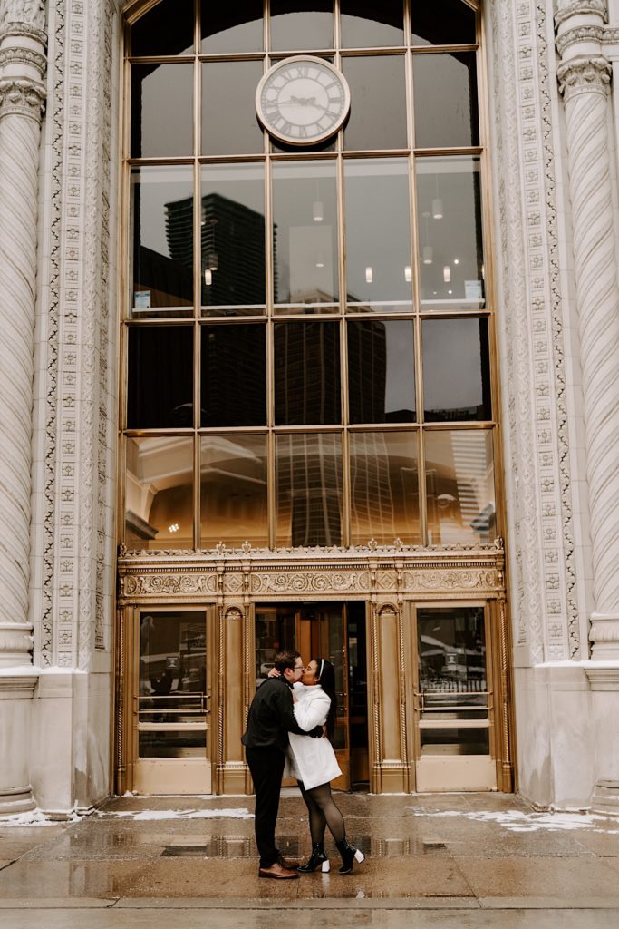 Engaged couple kissing in front of golden bronze doors