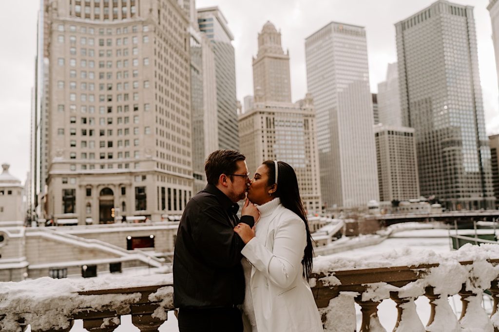Engaged couple kissing on snowy Chicago riverwalk