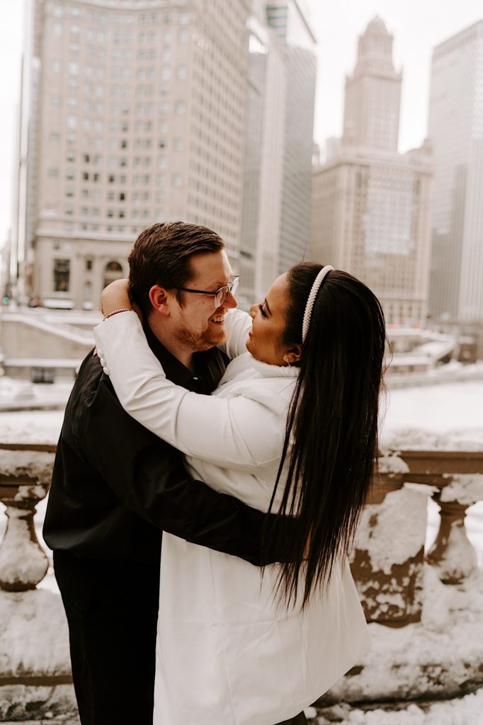 Bride and groom to be smiling at each other while embracing on Chicago riverwalk