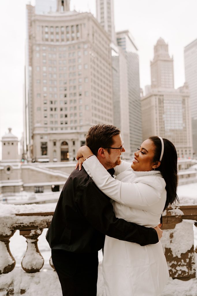 Bride and groom to be smiling at each other while embracing on Chicago riverwalk