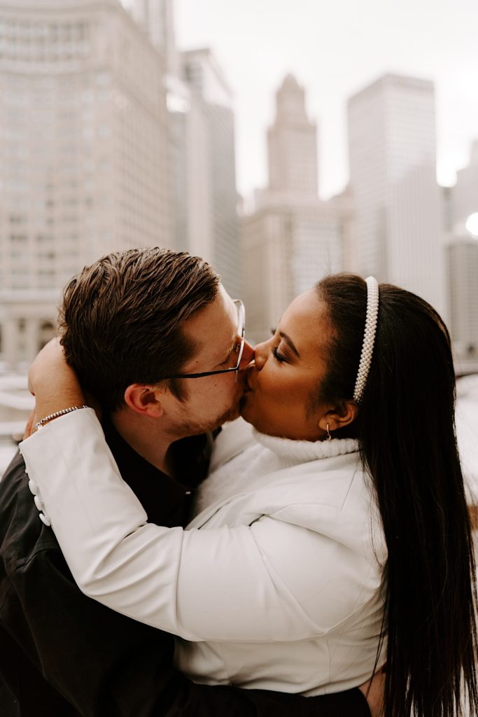 Bride and groom to be kissing while embracing on Chicago riverwalk