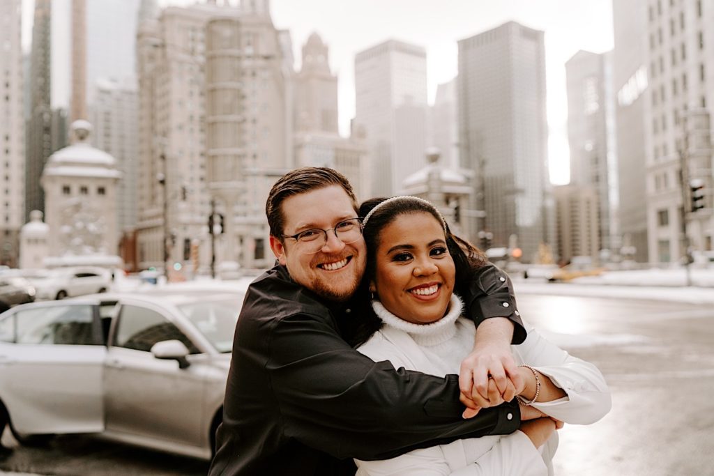 Fiance hugs bride to be from behind while smiling in downtown Chicago