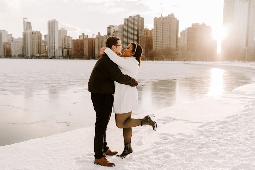 Engaged couple embraces on Chicago riverfront with skyline behind them