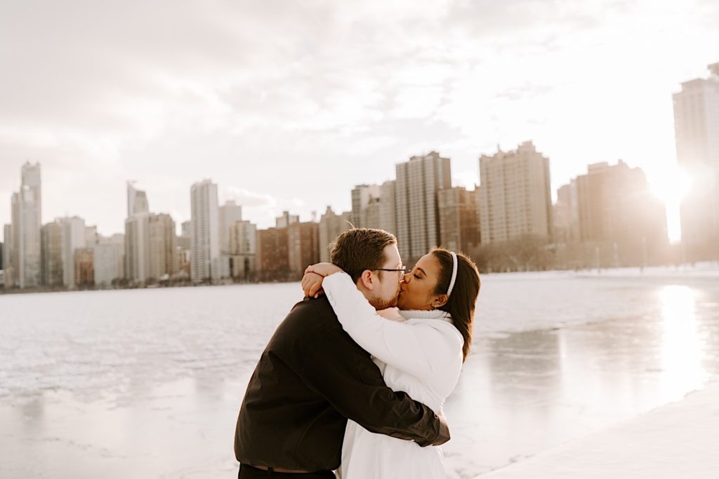 Engaged couple kisses on Chicago riverfront with skyline behind them