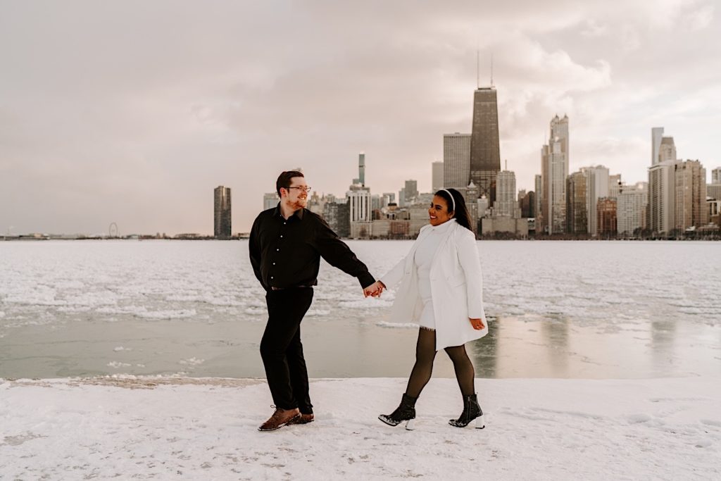 Engaged couple holding hands and on North Avenue beach in Downtown Chicago with the skyline behind them