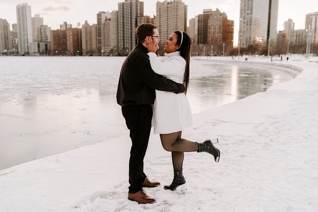 Engaged couple smiles at each other while hugging on North Avenue beach in the winter