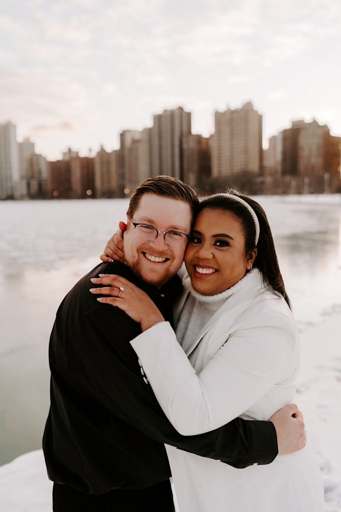 Engaged couple smiles while hugging on North Avenue beach in the winter