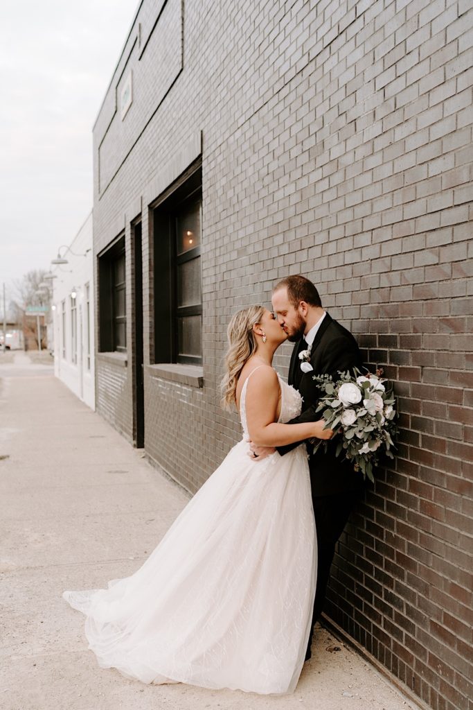 Newlyweds kiss against brick wall outside of ceremony in downtown Indianapolis
