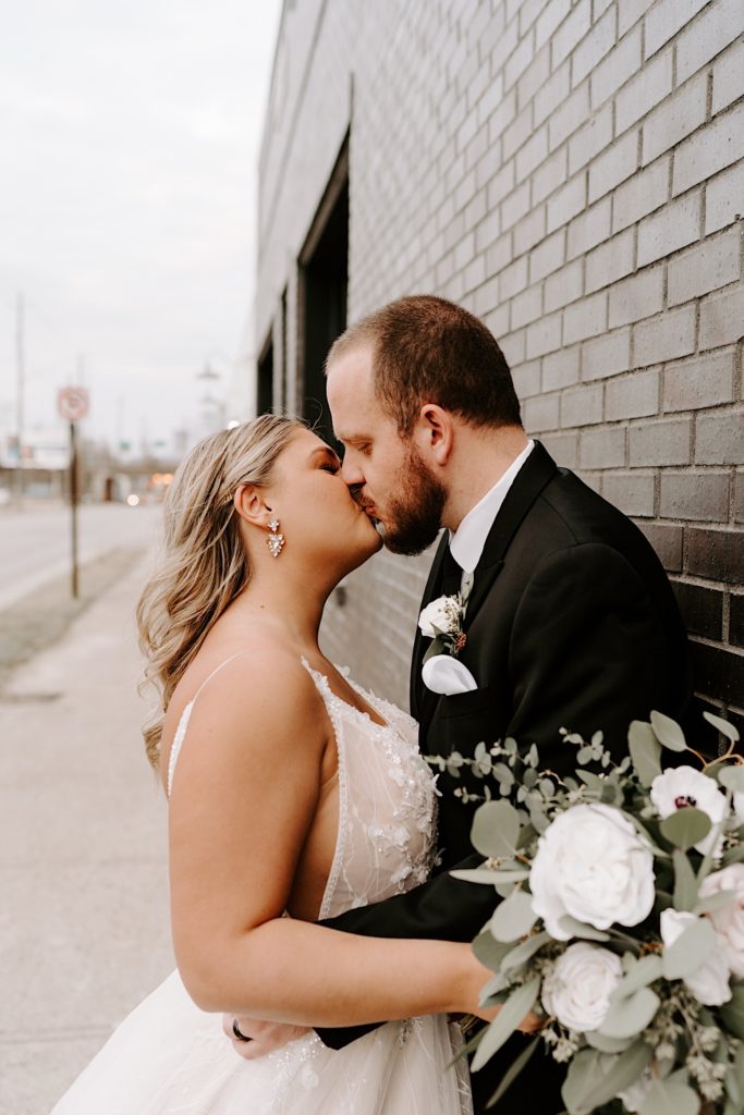 Newlyweds kiss against brick wall outside of ceremony in downtown Indianapolis