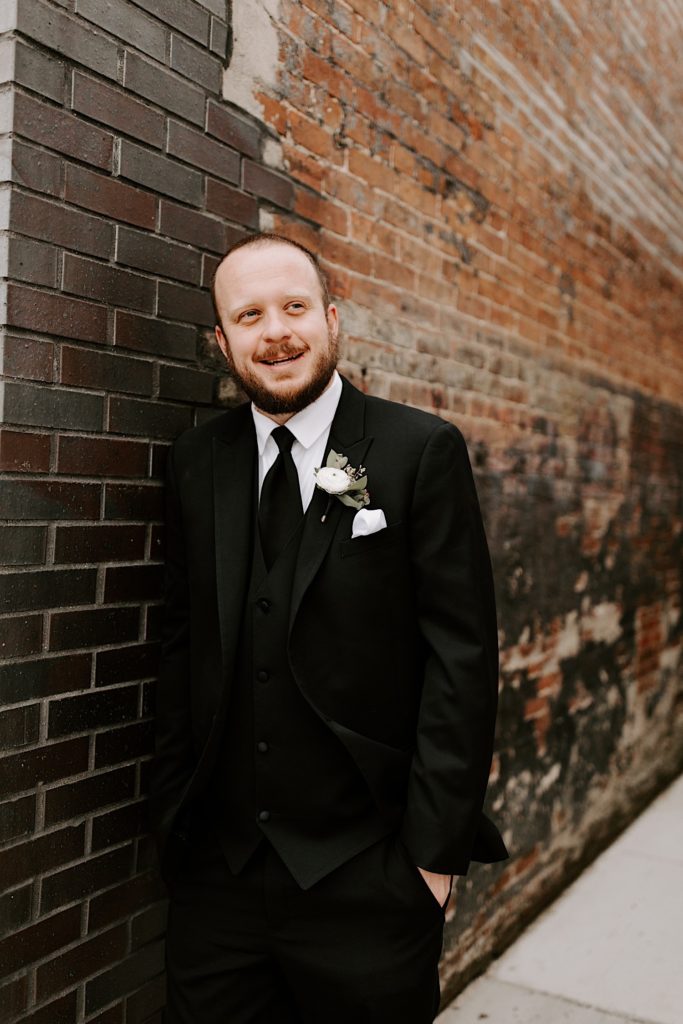 Groom in front of a brick wall outside of wedding venue in downtown Indianapolis