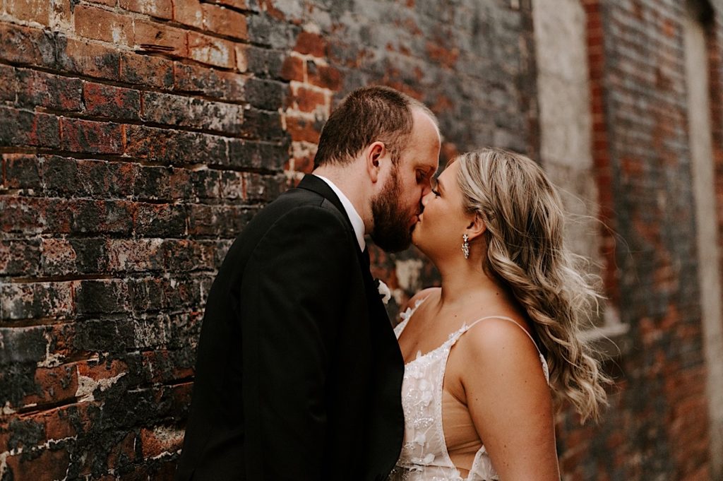 Newlyweds kiss in front of brick wall in downtown Indianapolis