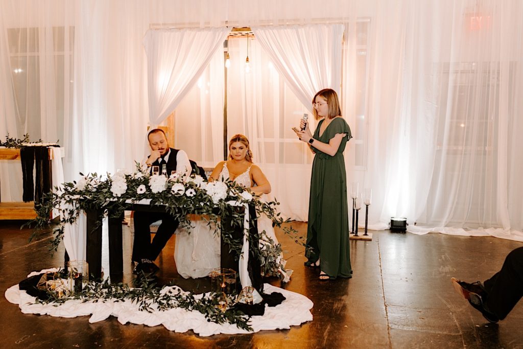 Newlyweds sitting at the sweetheart table while bridesmaid gives speech