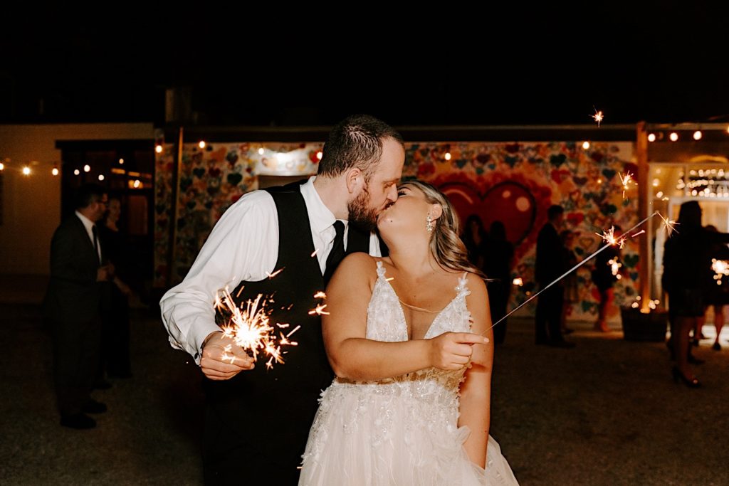 Newlyweds kissing and holding sparklers outside Ivory Foundry wedding reception
