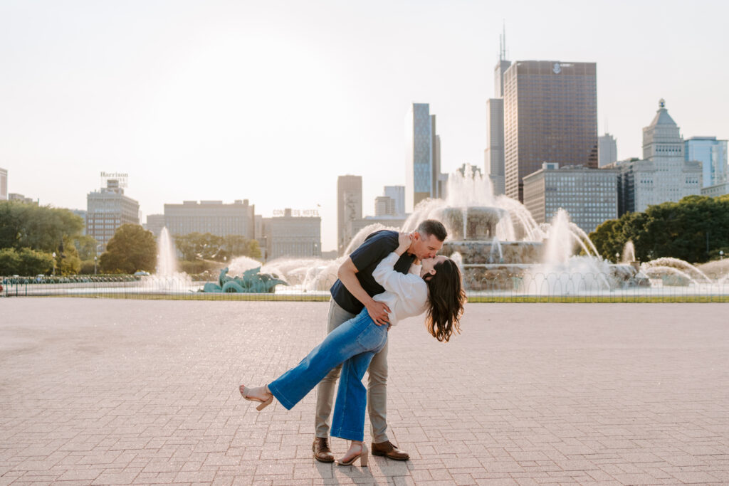 A man dips and kisses his fiancée in front of Buckingham fountain in Chicago during their engagement photos.