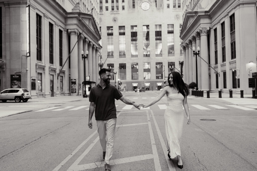 A couple walks while holding hands in the middle of a street outside of the Chicago board of trade building.