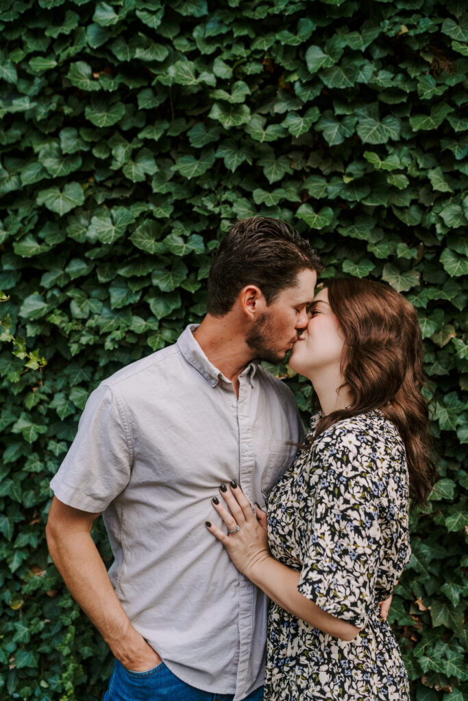 A couple kisses in front of a vine covered building in Chicago during their engagement session.
