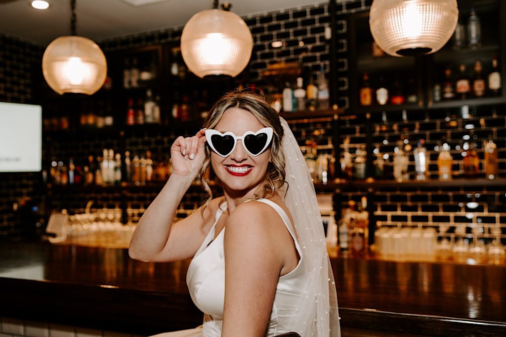 Bride wears heart sunglasses in front of bar in intimate Chicago wedding venue