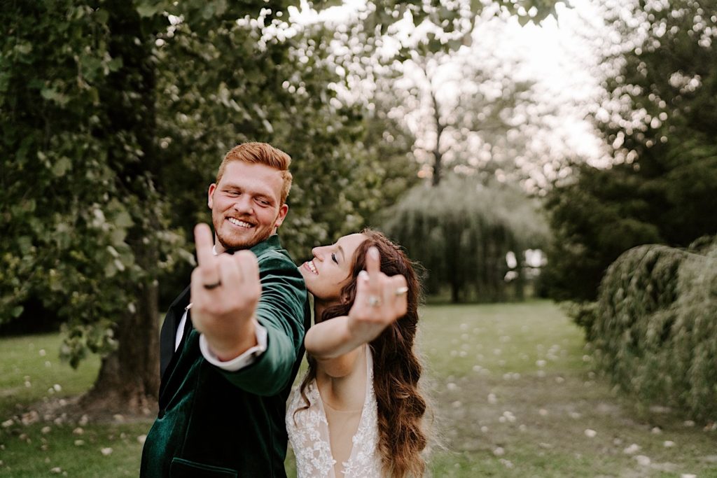 Groom in an emerald green suit and bride in a floral dress showing off their wedding rings.