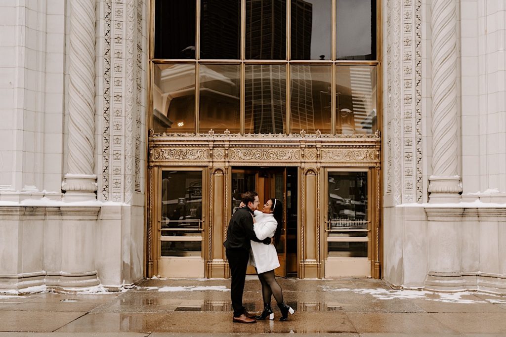 Engaged couple embrace in front of the Tribune building doors 
