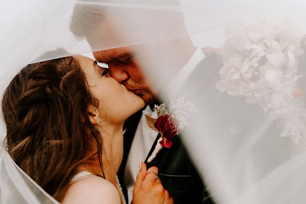 Bride and groom take their wedding portraits kissing underneath the brides veil.
