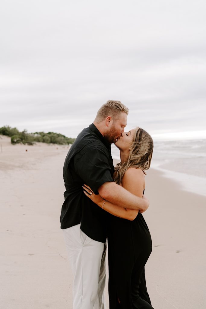 Couple kisses during their engagement session on the beach at the Indiana Dunes.