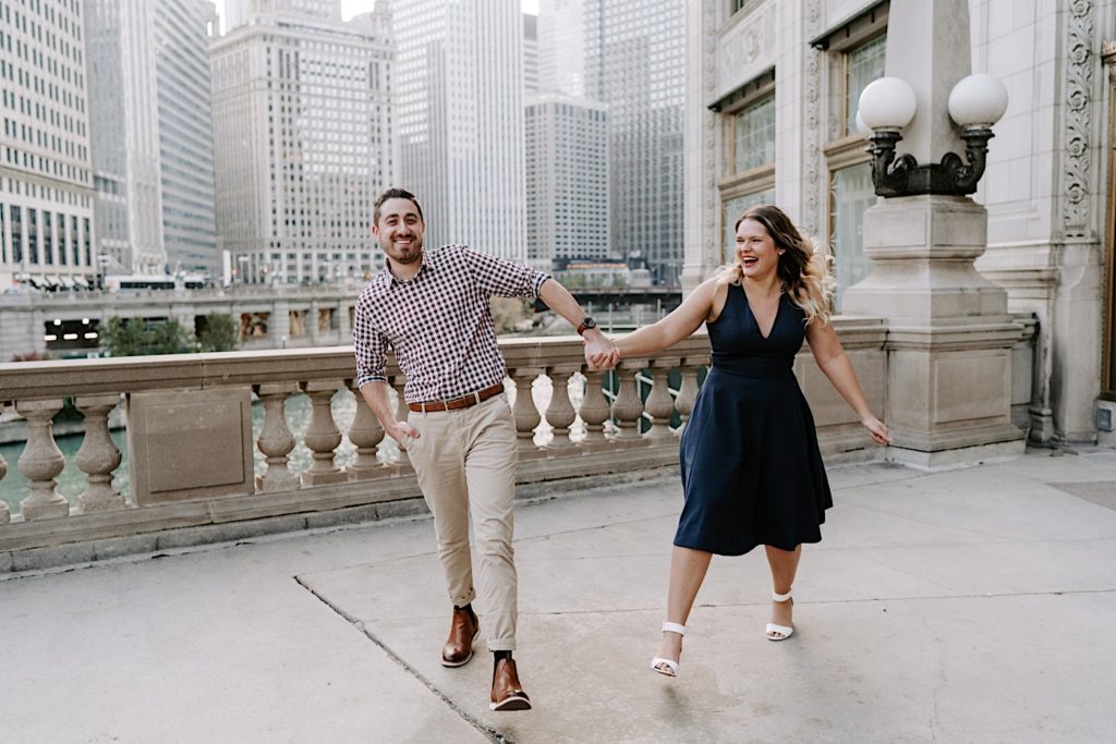 Couple walks while holding hands towards the camera in front of the Tribune Tower.