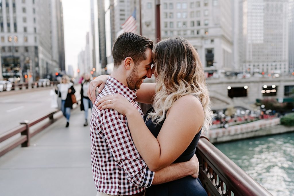 Couple holding each other while standing on a bridge over the Chicago River during their engagement session.