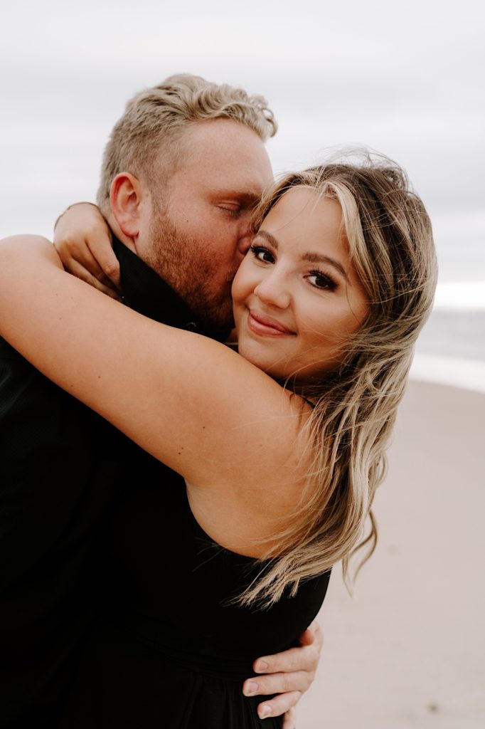 Couple kisses on the beach during their summer engagement session in Indiana.