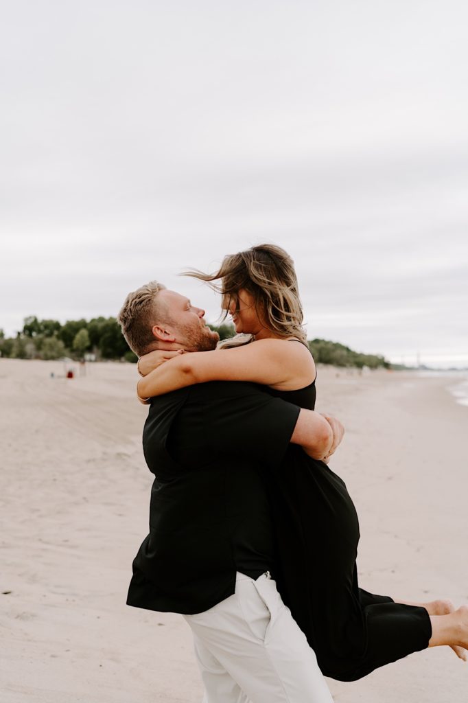 Couple spins while holding each other  on the beach during their engagement session.  