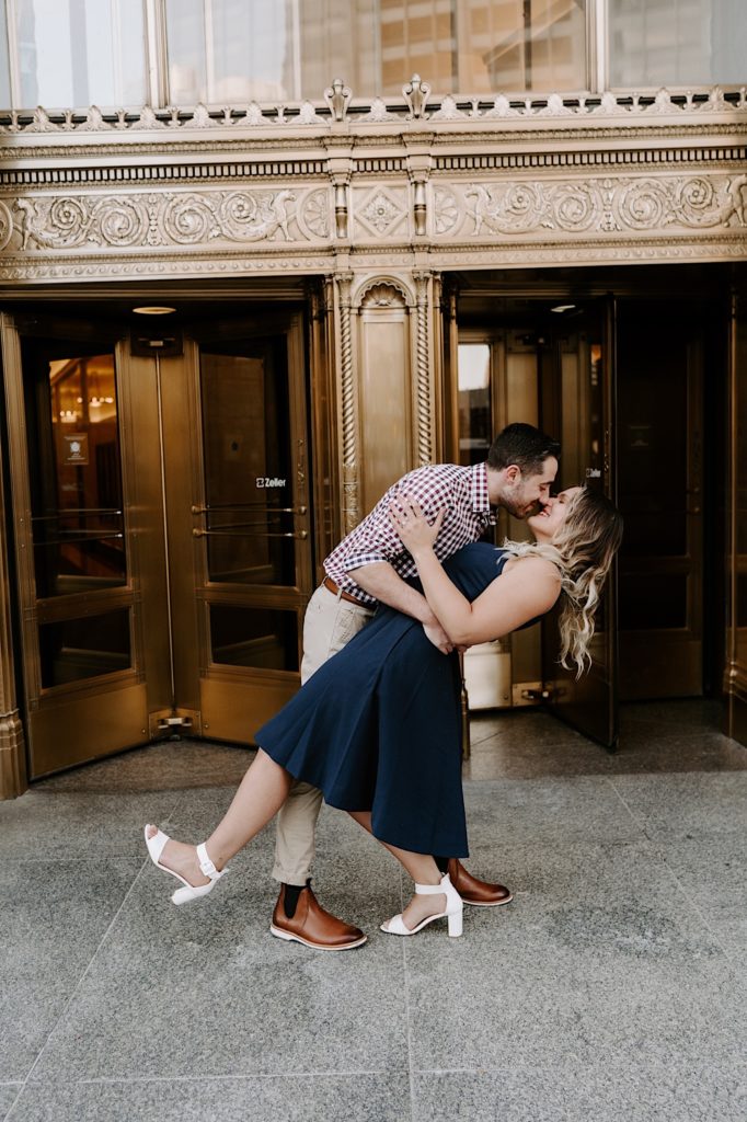 Couple dips and kisses during their engagement session in front of the Tribune towers in Chicago